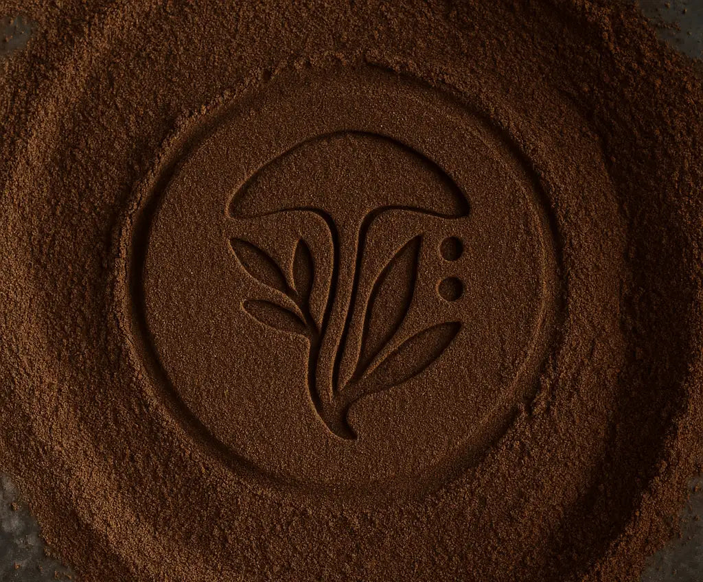 A circular, dark brown powder imprint featuring a stylized mushroom and leaf design.