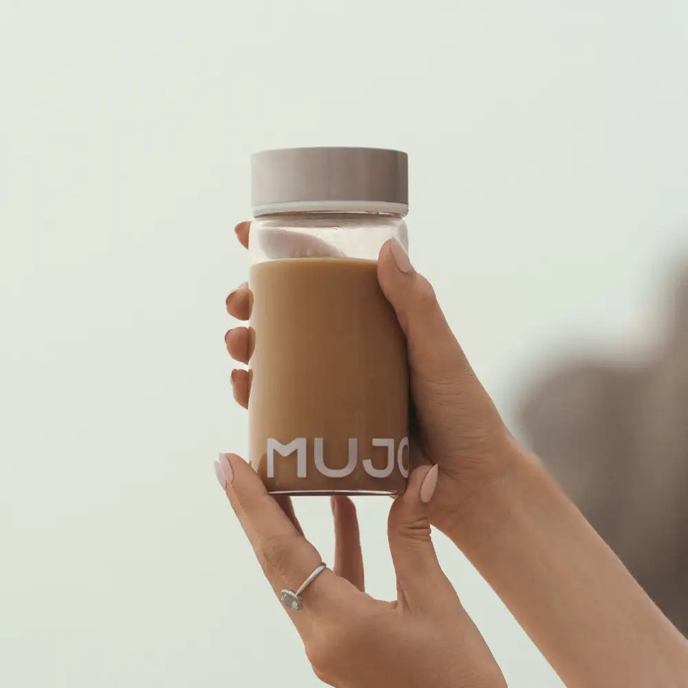 A clear glass muji travel mug with a silver lid, filled with brown liquid.