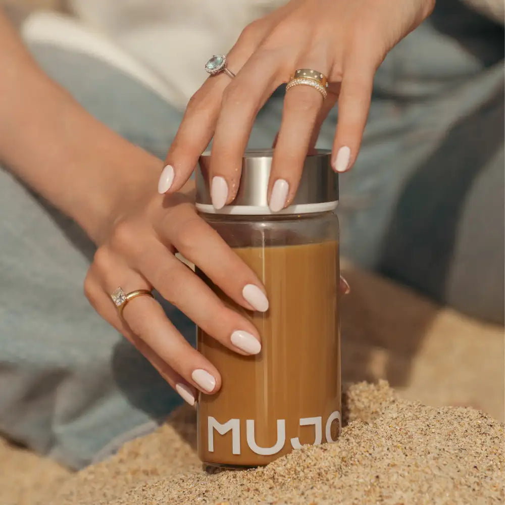 Clear glass mujo travel mug with a silver lid and white lettering, filled with coffee.
