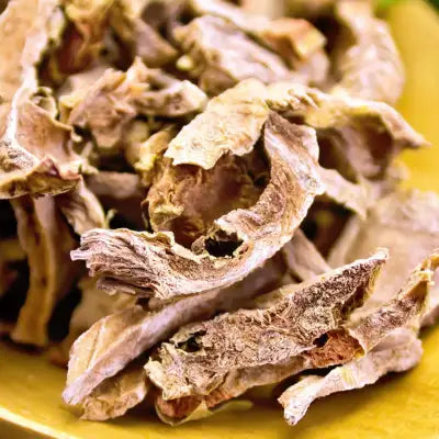 Dried, brittle root slices with a rough texture and earthy brownish-purple hue.