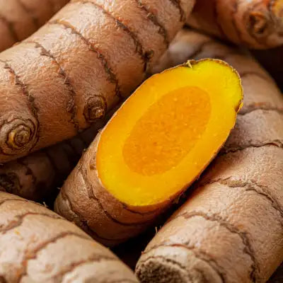 A vibrant yellow-orange turmeric root with a rough, brownish skin and a smooth, bright interior.